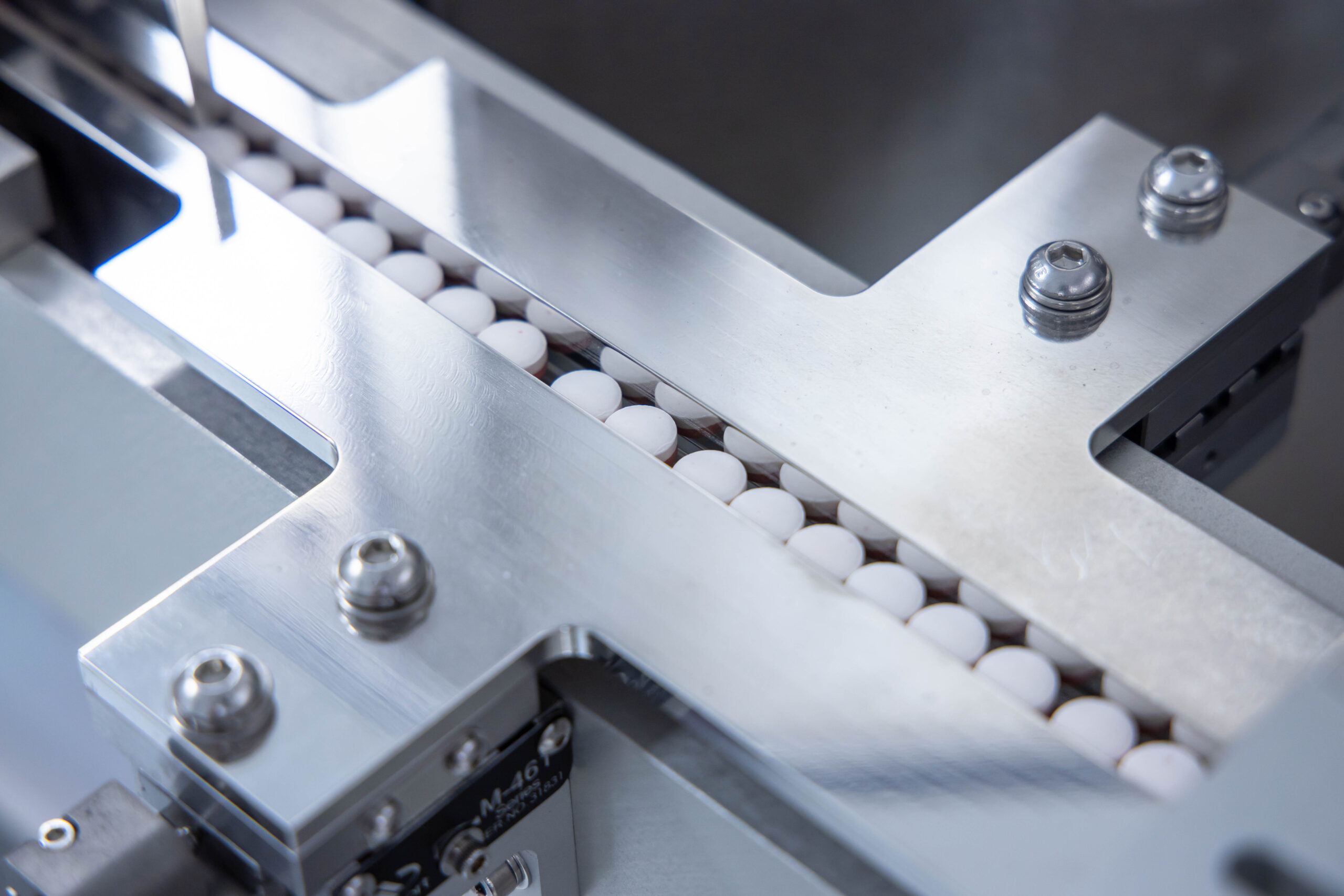 Undrilled tablets sitting on laser conveyor track in a compact line